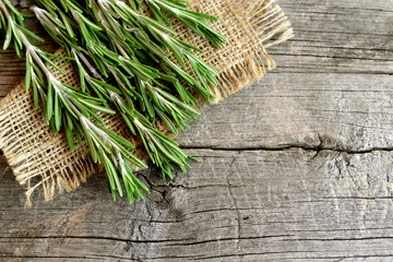 Green sprigs of fresh rosemary on the burlap and old wood background with blank space for text....