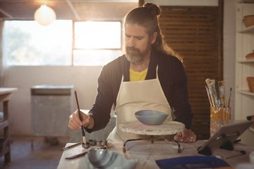 Attentive male potter painting on bowl