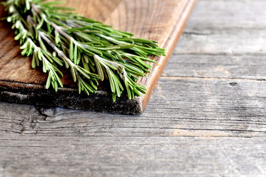 Raw green rosemary sprigs on a kitchen board and an old wooden background with empty space for text. Aromatic herb used in cooking, medicine, cosmetics. Closeup