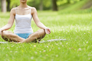 Yoga woman siting on grass meditaiting in lotus position.