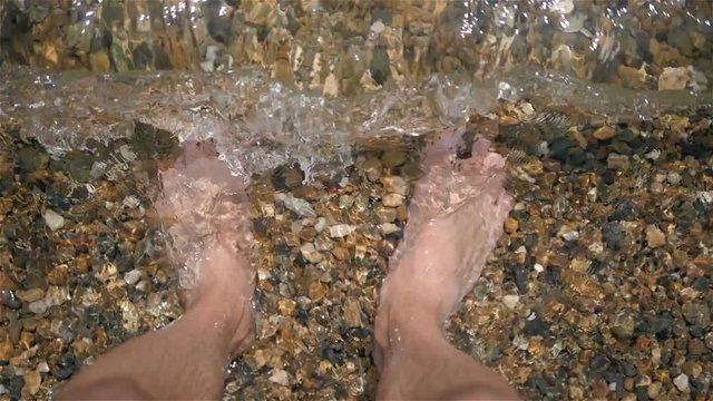 Male Feet On Pebbly Beach On a Sunny Day, POV