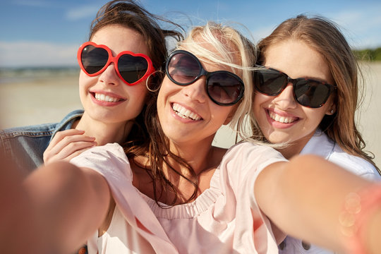 group of smiling women taking selfie on beach
