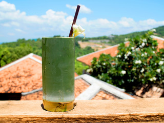 Local traditional fruit juice in handmade glass made from bamboo with natural view and blue sky in background. Folk wisdom.