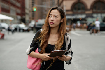 Young Asian woman in city using tablet computer
