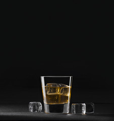whiskey in clear glass, ice, against a dark background 