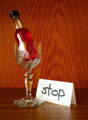 Glass, bottle with alcohol and paper with text STOP. Appeal to overcome addictive alcohol abuse and dependence through detoxifiction, treatment, rehabilitation and abstinence  - obrazy, fototapety, plakaty