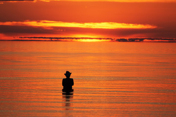 Naklejka na ściany i meble Silhouette of a fisherman in the sea at sunset