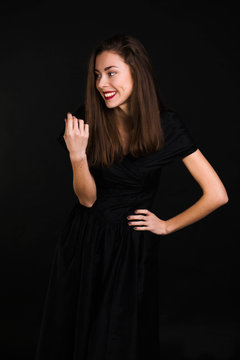 Girl standing in a black dress is laughing and looking away