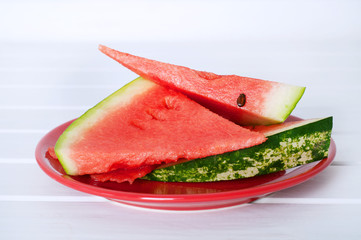 Watermelon slices on red porcelain plate on white wooden table