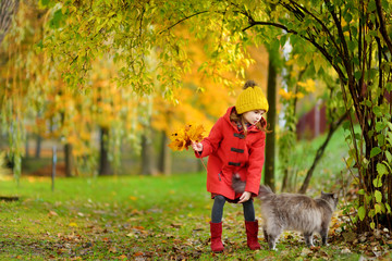 Portrait of a cute little girl and her pet cat on beautiful autumn day