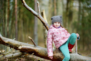 Funny little girl sitting on a log during forest hike