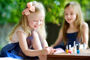 Obraz na płótnie Canvas Adorable little girls having fun playing at home with colorful nail polish doing manicure and painting nails