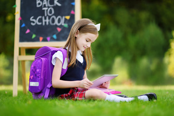 Adorable little girl using computer tablet while sitting on a grass on summer day