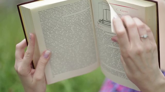 Reading a book. Beautiful female lying on the grass and reading a book in her hands.