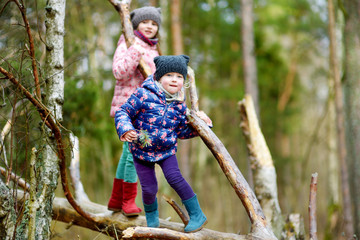 Naklejka na ściany i meble Two funny little sisters sitting on a log during forest hike