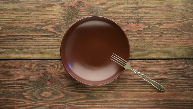 Brown empty dinner plate with fork and knife on wooden table 
