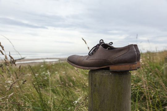 Discarded or lost pair of mens brown leather shoes left on top of wooden post at coastal site.