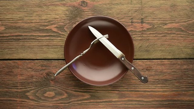 Brown empty dinner plate with fork and knife on wooden table 
