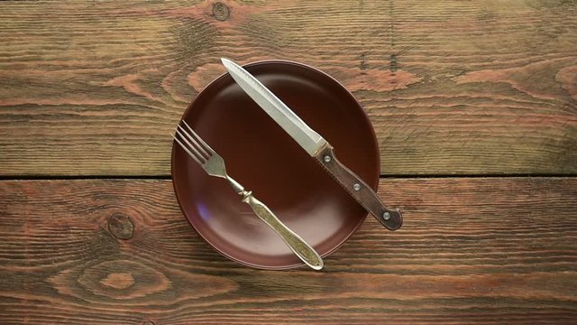 Brown empty dinner plate with fork and knife on wooden table 
