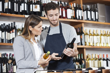 Salesman Showing Wine Bottle To Female Customer