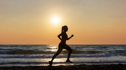 Fototapeta na wymiar Silhouette einer laufenden Frau am Strand bei Sonnenuntergang