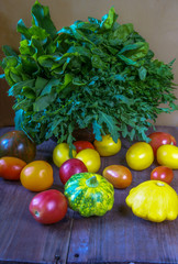 The big basket with basil, arugula and spinach on a wooden table. In the foreground - vegetables, tomatoes and bush pumpkins