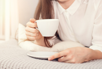 Fototapeta na wymiar beautiful young woman hold cup of coffee lying think relaxing on the bed, bed home indoors, happy smile day dreaming with tea mug in hands looking up away in thought 
