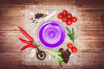 Fresh tomatoes, chili pepper and other spices and herbs around modern white square plate in the center of wooden table and cloth napkin. Top view. Blank place for your text. Horizontal.