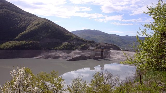 View on hydroelectric power station surrounded by verdant mountains on the background of clouds and blue sky. Zhinvali Dam, the river Aragvi, Georgia, Caucasus.

