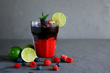 Raspberry and blueberry smoothie in glass, decorated with blueberries, mint and lime on a gray background