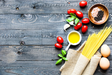 Top view of italian ingredients for tomato and basilic spaghetti with olive oil and garlic over a wood background.