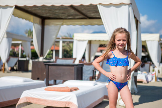 Adorable happy smiling little girl on beach vacation near sunbeds