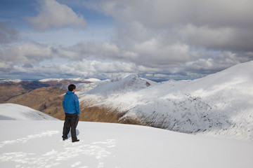 Fototapeta na wymiar A man standing on top of a mountain admiring the view of Scottish mountains covered in snow.