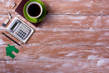 Office table desk with supplies, white blank note pad, cup, pen, pc, crumpled paper, flower on wooden background. Top view