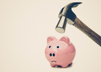 A sad pink piggy bank is about to be hit by a hammer