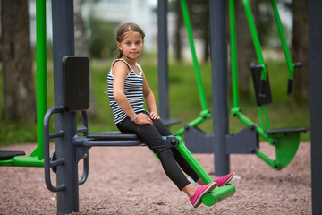 Fototapeta na wymiar Little girl sitting on a public trainer-machine on the Playground.