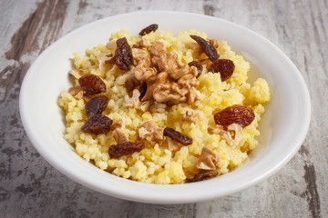 Cooked millet groats with raisins and walnuts on white plate, healthy food and nutrition