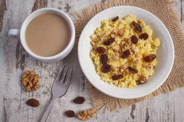 Cooked millet groats on white plate and cup of coffee with milk, healthy food and nutrition