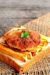 Sandwich with fried potatoes and minced meat cutlet on a burlap and on old wooden table. A sandwich cooked from slice of white bread, deep fried potatoes and Turkey cutlet 