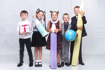 Cheerful schoolgirls and boys stand together and hold a huge pencil