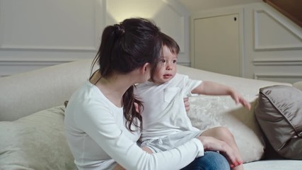 Mother sitting on the bed and holding her playful little son on her knees