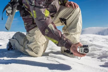 Fotobehang a man filming with action camera in snowy mountain range © karelian