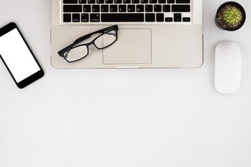 White office workspace with blank screen smartphone, eyeglasses, mouse and laptop.  Top view with copy space