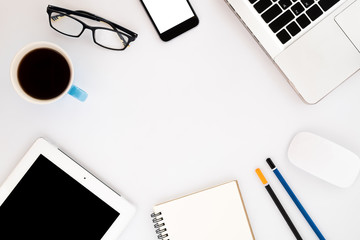 White office desk table with laptop,pencils,blank screen smartphone,tablet,leather notebook,eyeglasses and cup of coffee. Top view with copy space.Business desk table concept.