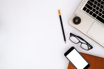 White office desk table with laptop, pencil, blank screen smartphone, eyeglasses,compass and leather notebook.Top view with copy space.Business desk table concept.