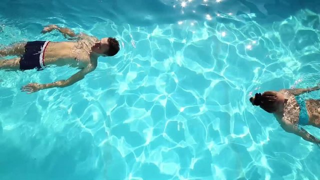 Couple has a rest in the pool with champagne. they are smiling, hugging and kissing.