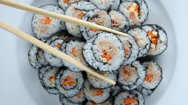 Close up of chopsticks holds sushi maki gunkan roll and place it on a plate or platter set. Served in Japanese bar restaurant. Top view, flat lay. Food background. copy space.  4K