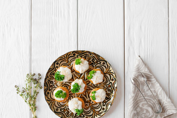 Crackers with cheese cream and parsley, free space, flat lay. Appetizing regale snack, served on beautiful plate on white wooden background. Copy space for text