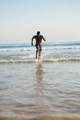 Fototapeta na wymiar Man training at the beach. Black athlete running into the sea for leg power training.
