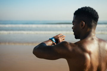 Black athlete timing outdoor beach running or swimming workout on smartwatch. Summer training at...